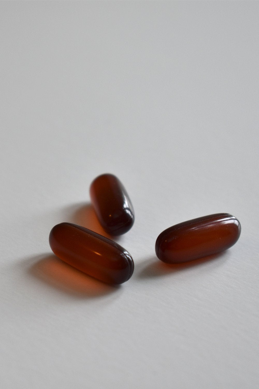 Close-up of three amber fish-oil softgel capsules on a plain white surface.